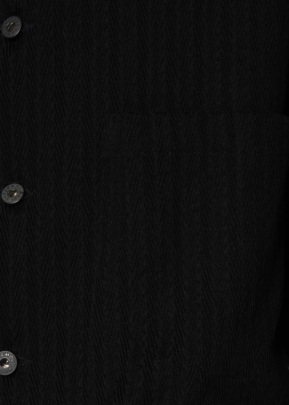 Close-up of a black textured knit fabric with three visible silver buttons along the left side.