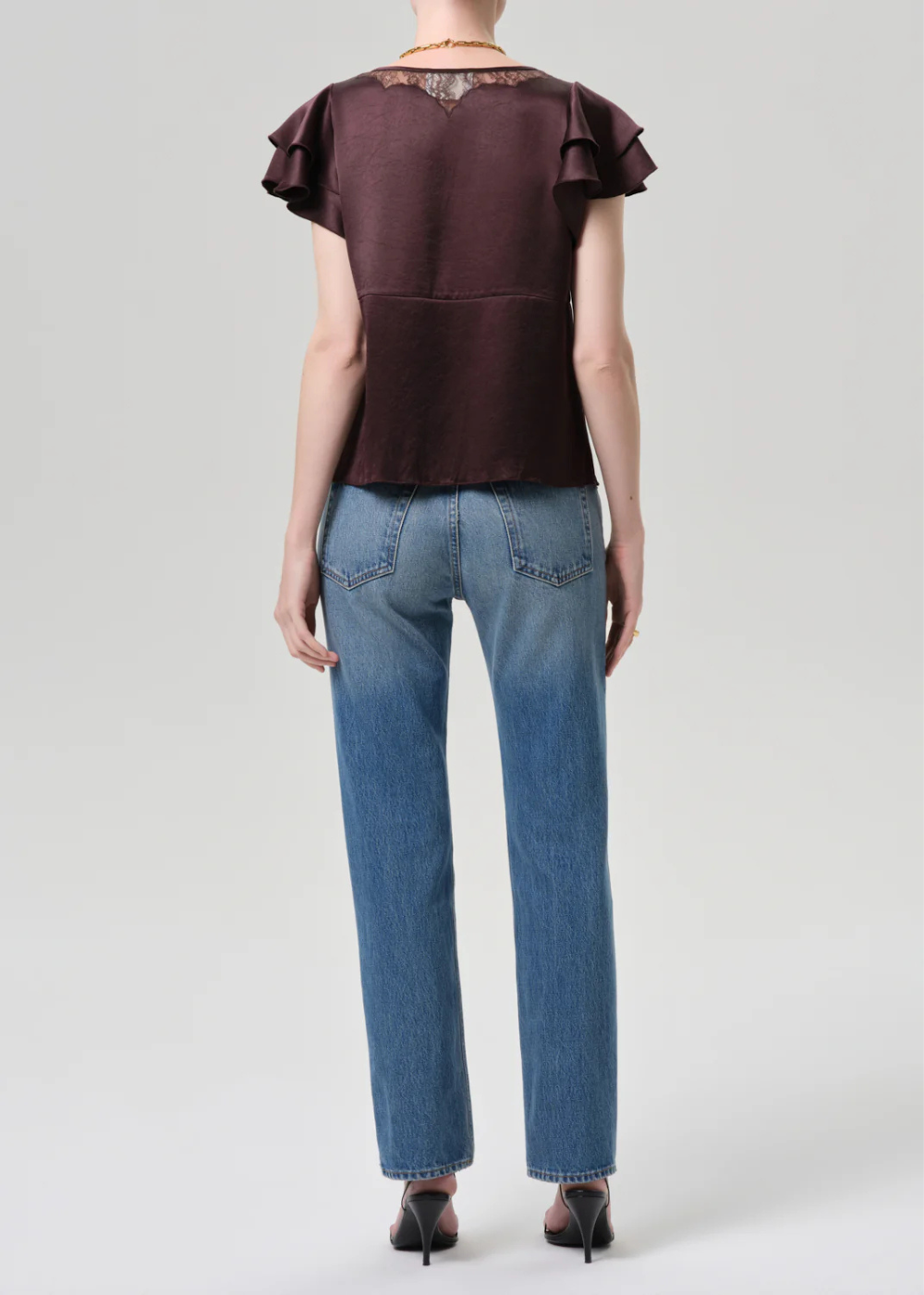 Person wearing a brown top with ruffled sleeves and blue jeans on a white background
