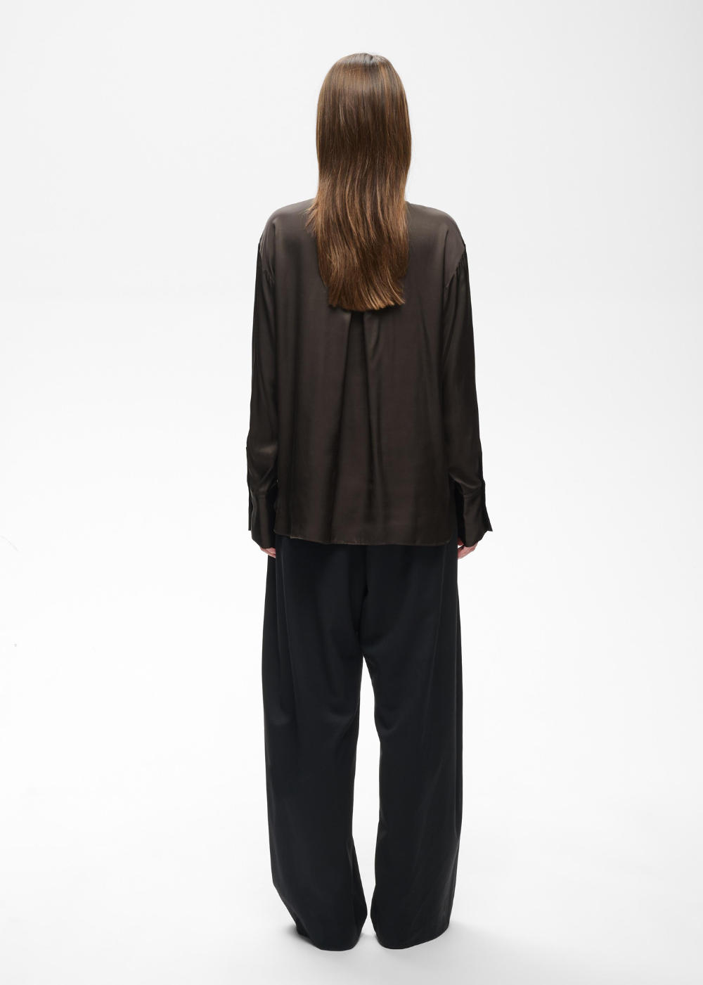 A model viewed from the back wearing a dark brown long-sleeve blouse and black wide-leg trousers against a plain white studio background.