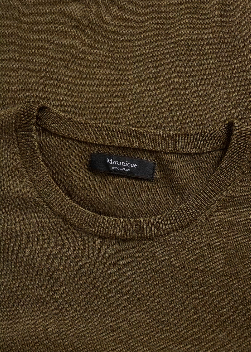 Close-up of a ribbed knit crewneck sweater in a dark olive brown color, showing a black neck label with the brand name 'Matinique'.