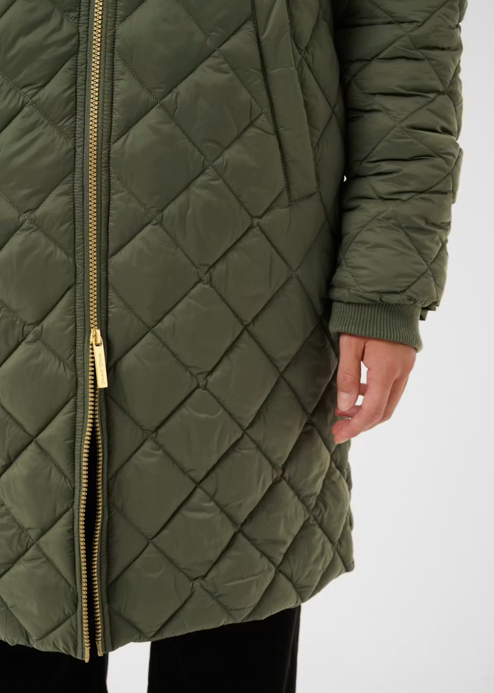 An olive green diamond-quilted puffer jacket with a gold-tone zipper, shown on a model against a plain white background.