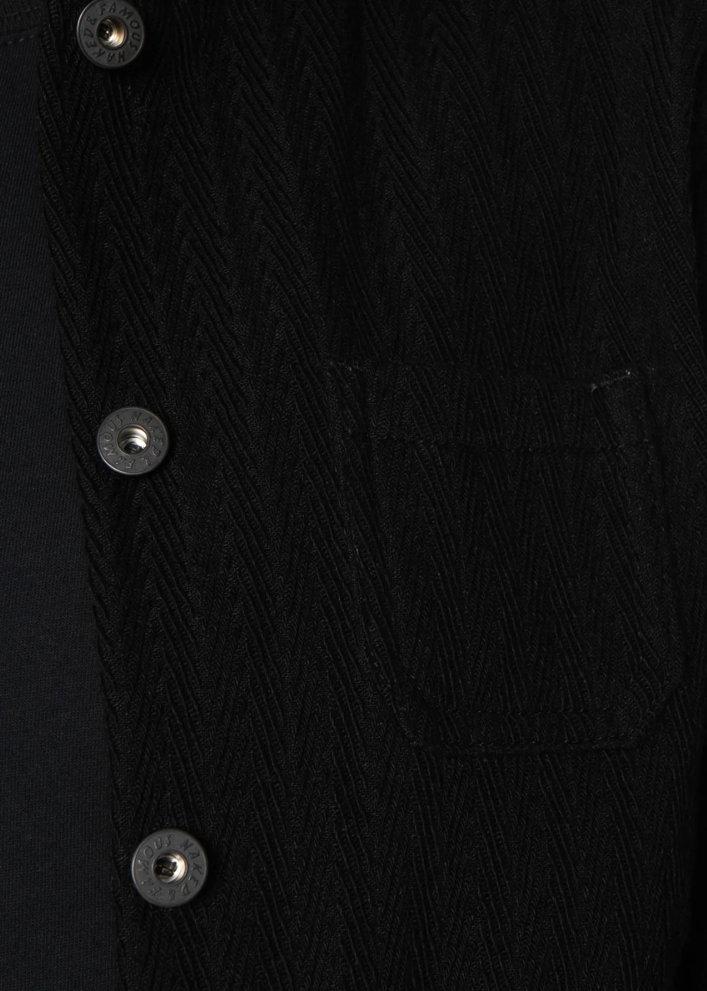Close-up of a black textured herringbone fabric garment with three visible metal buttons on the front.