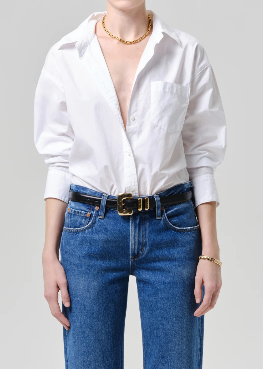Person wearing a white blouse and blue jeans with a gold belt on a gray background