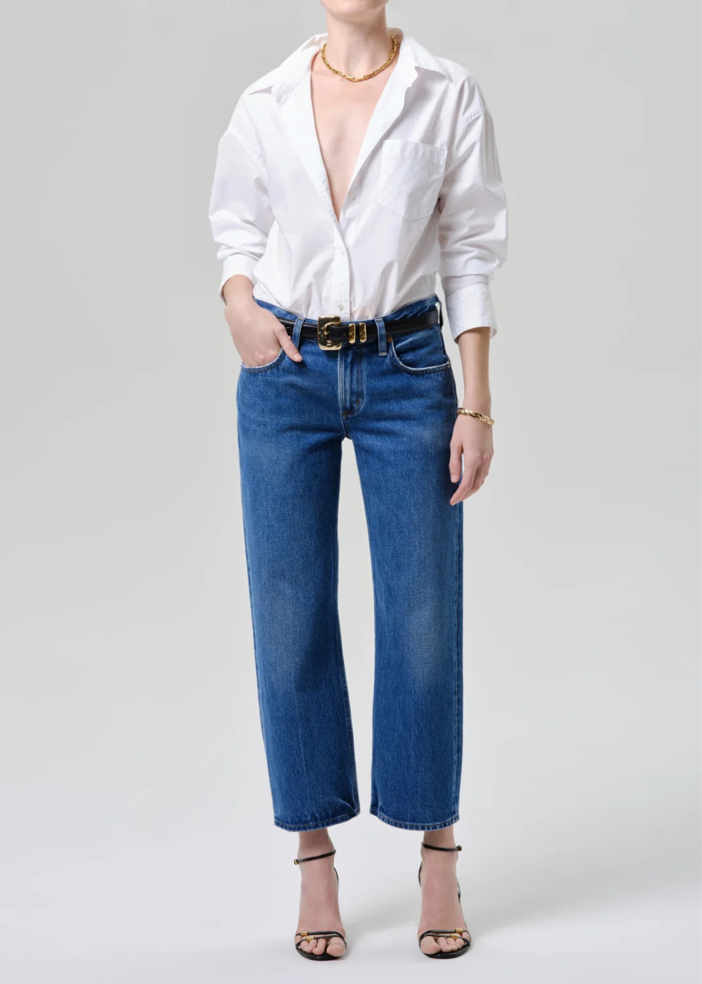 Person wearing a white shirt, blue jeans, and a gold belt on a plain background