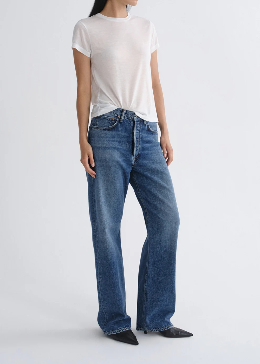 A model wearing a white short-sleeve t-shirt and blue wide-leg jeans, standing against a light gray studio background.