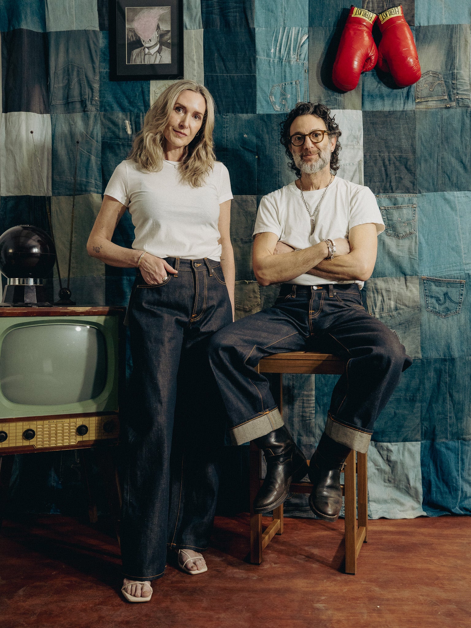 Two people sitting in a room with a patchwork wall, vintage television, and boxing gloves.
