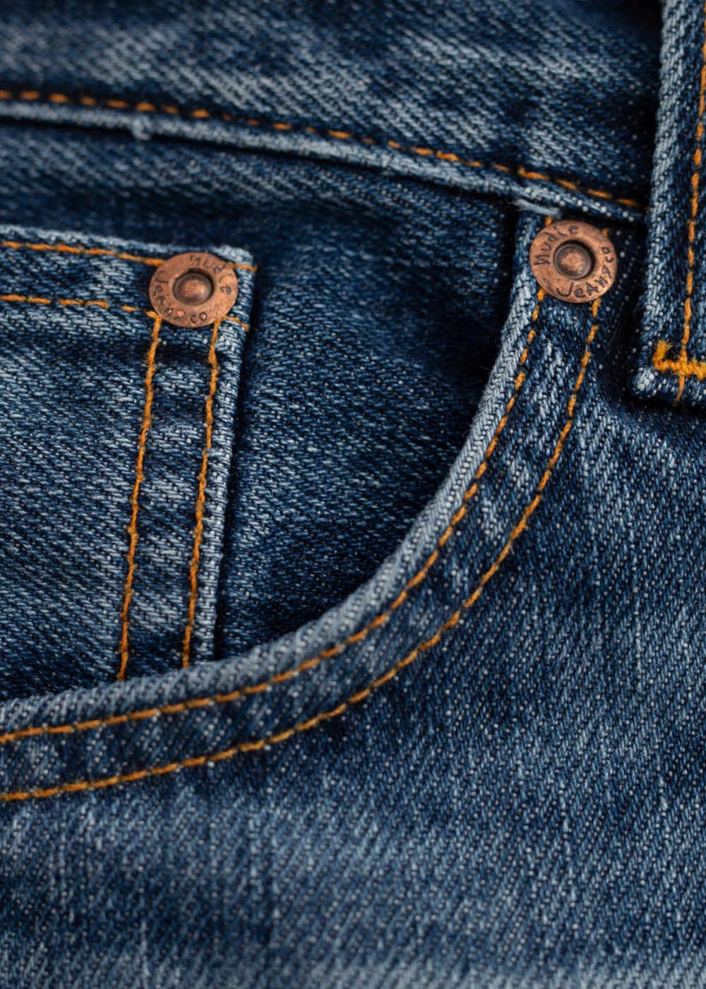 Close-up of a blue denim pocket with orange contrast stitching and copper-toned metal rivets.
