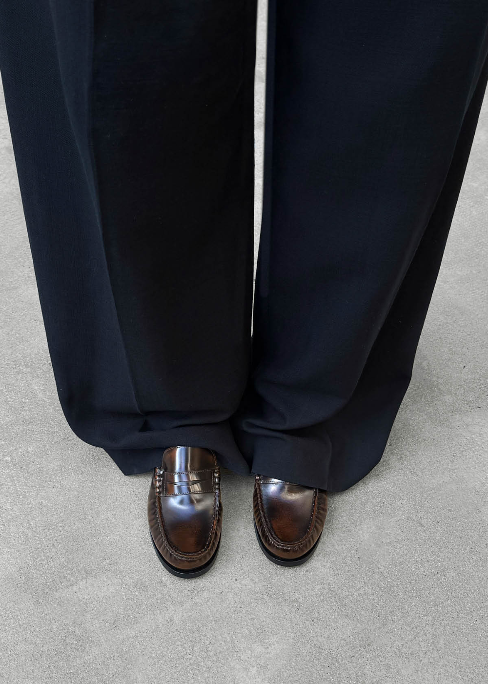 Person wearing dark blue pants and brown shoes on a gray surface