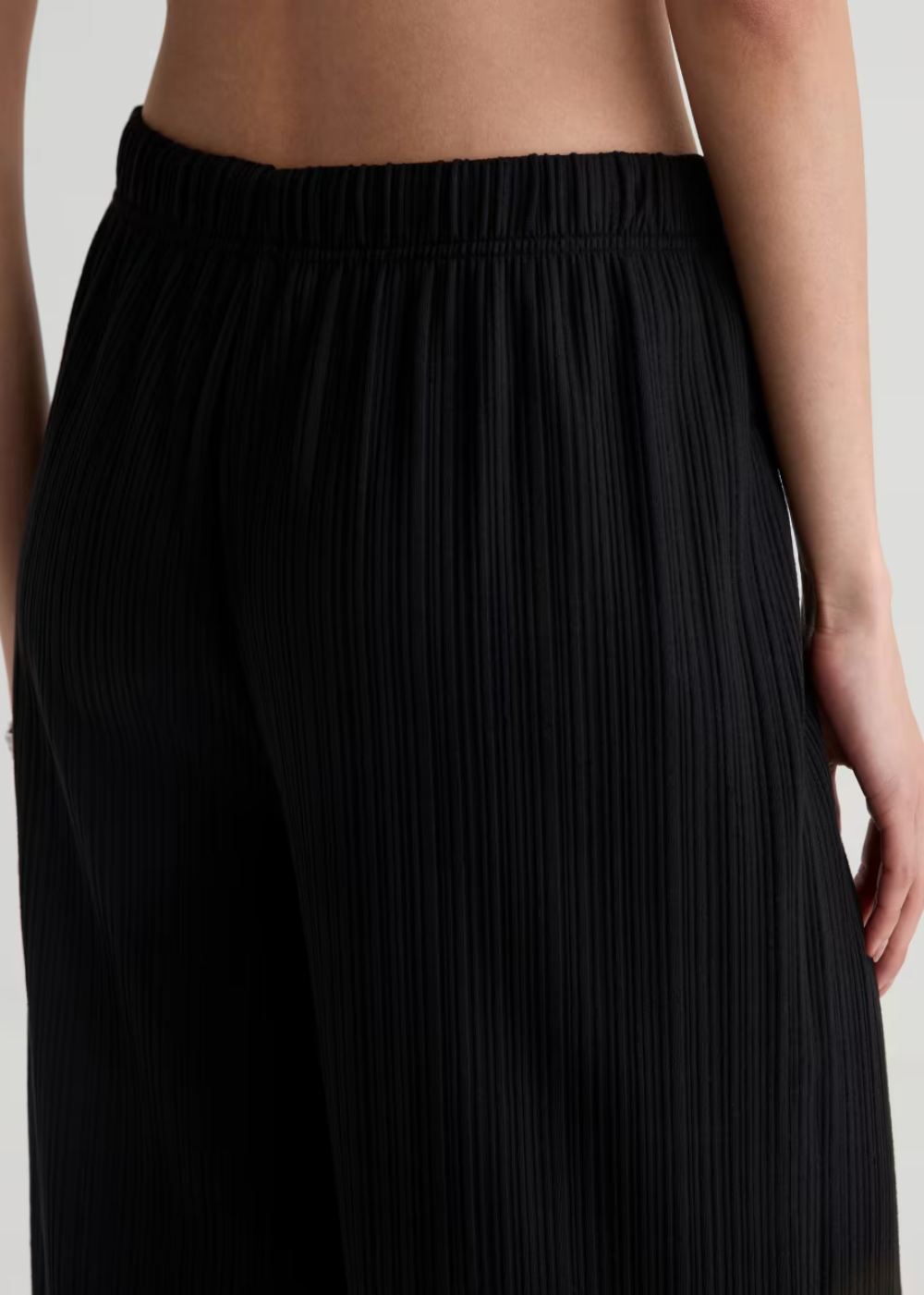 Close-up of a model wearing black pleated wide-leg pants, showing the textured fabric and elastic waistband.