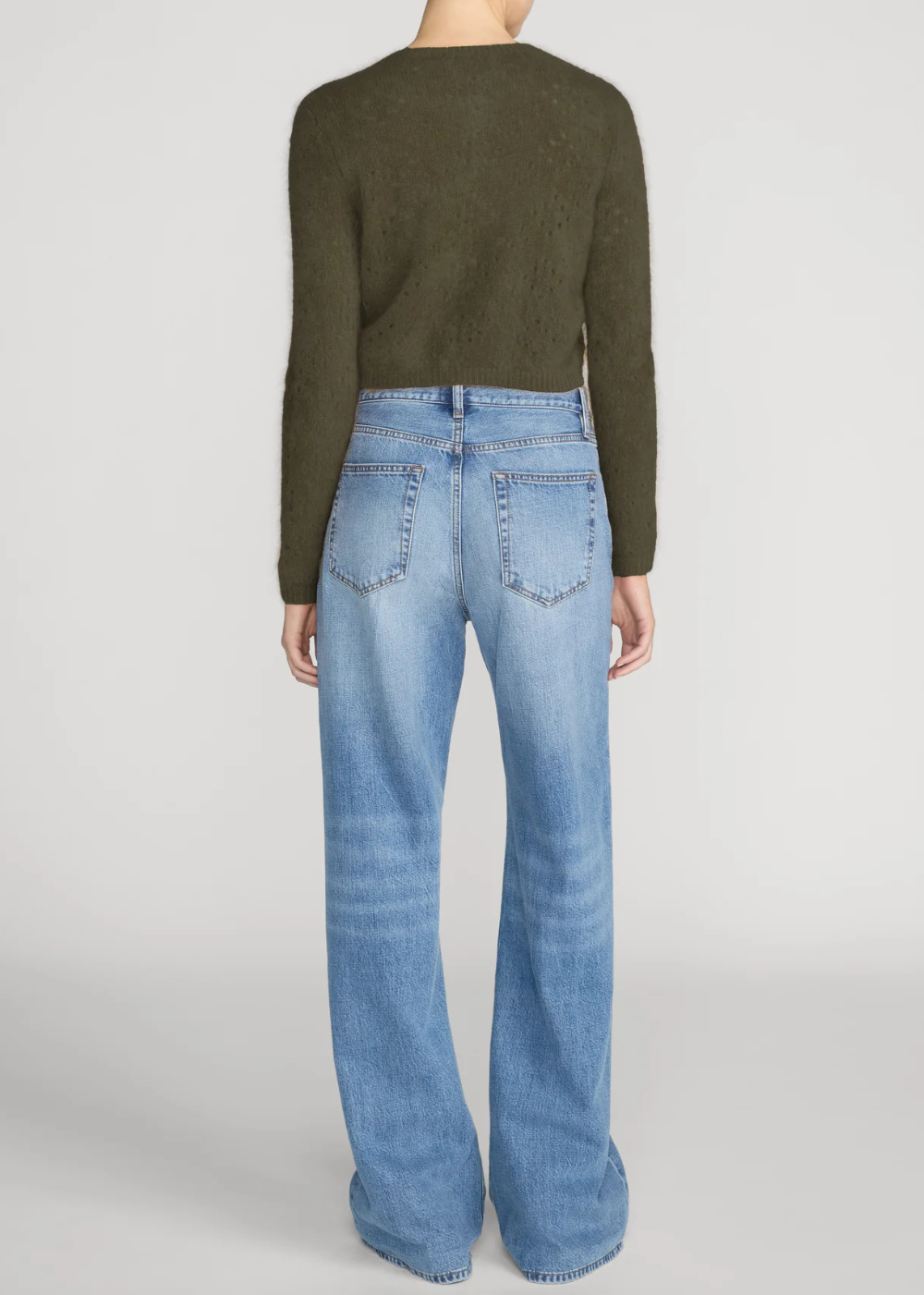 A model shown from the back wearing a dark olive green long-sleeve knit top and light-wash blue wide-leg jeans against a light gray studio background.