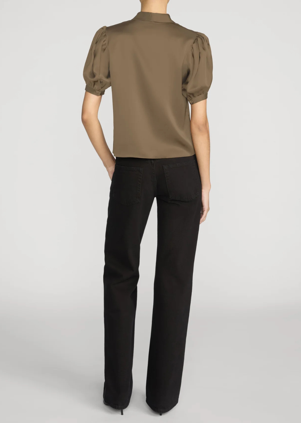 A model shown from the back wearing a short-sleeved, high-neck satin blouse in a muted olive-brown color paired with black trousers, against a light gray studio background.