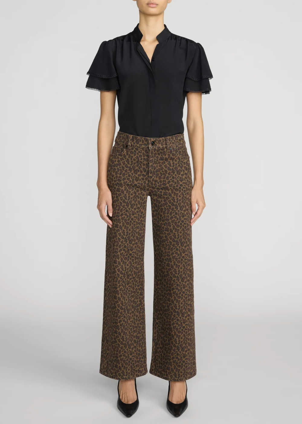 A model wearing a black short-sleeve blouse with ruffled sleeves and high-waisted brown leopard-print wide-leg trousers, paired with black pointed-toe heels, against a light gray studio background.