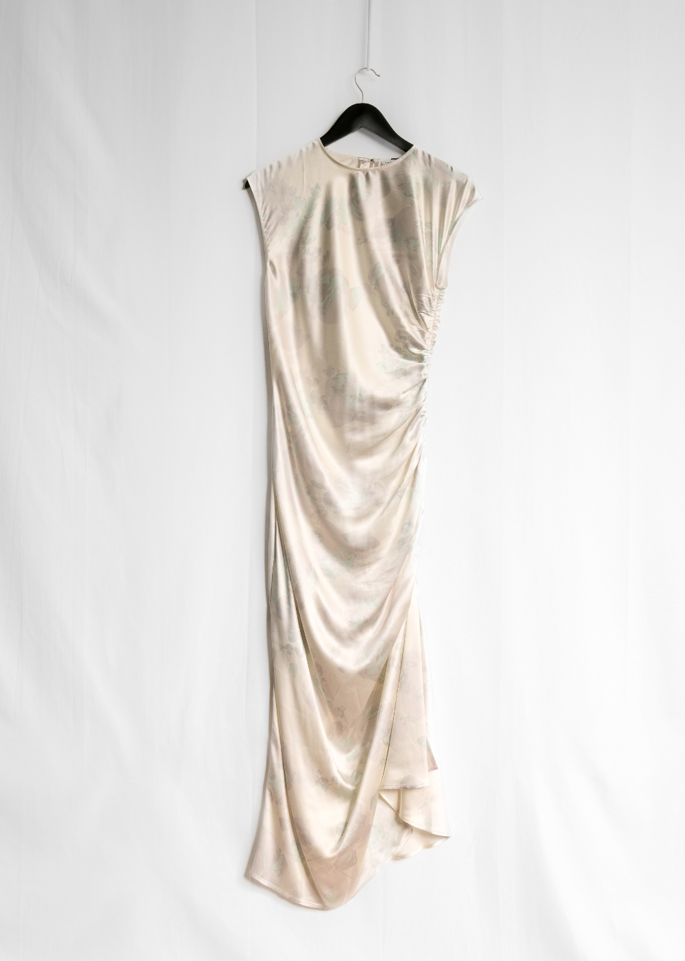 A sleeveless champagne-colored satin maxi dress with draped ruching, hanging on a black hanger against a white fabric backdrop.