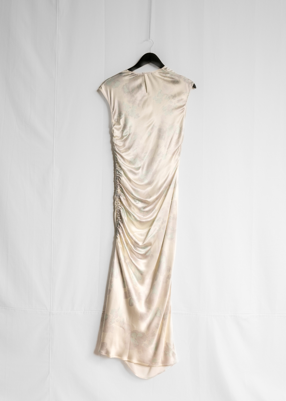 A champagne-colored satin slip dress with ruched detailing, hanging on a black hanger against a white fabric backdrop.