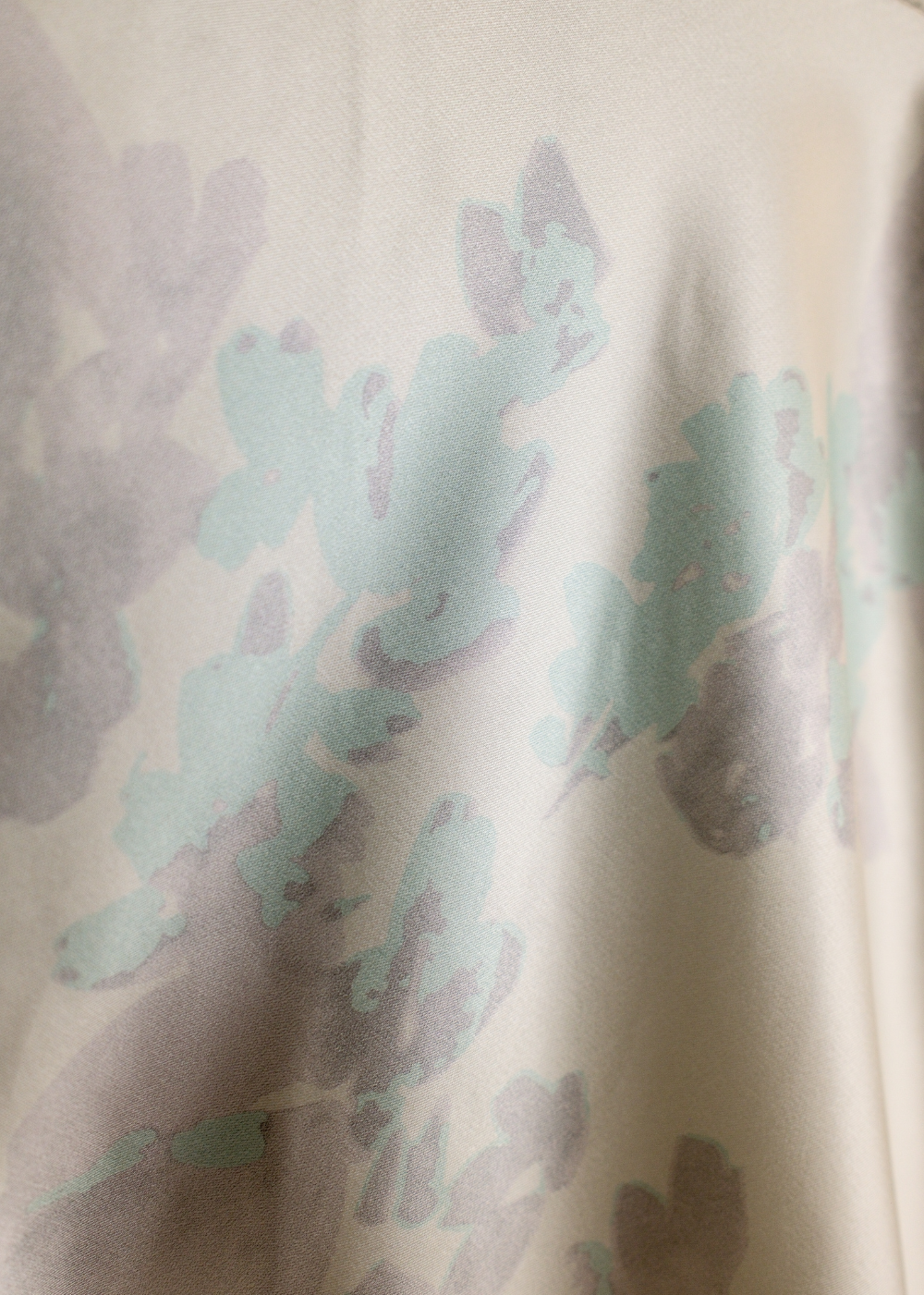 A close-up of a soft cream-colored fabric with an abstract watercolor-style print in pale mint green and muted taupe.