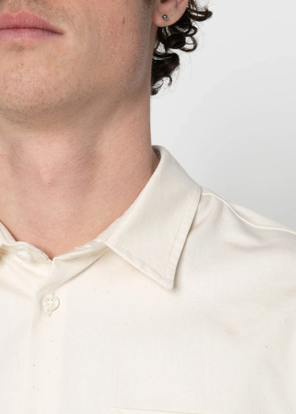 Close-up of a person wearing a light cream or off-white button-up shirt with a pointed collar, against a plain light background.