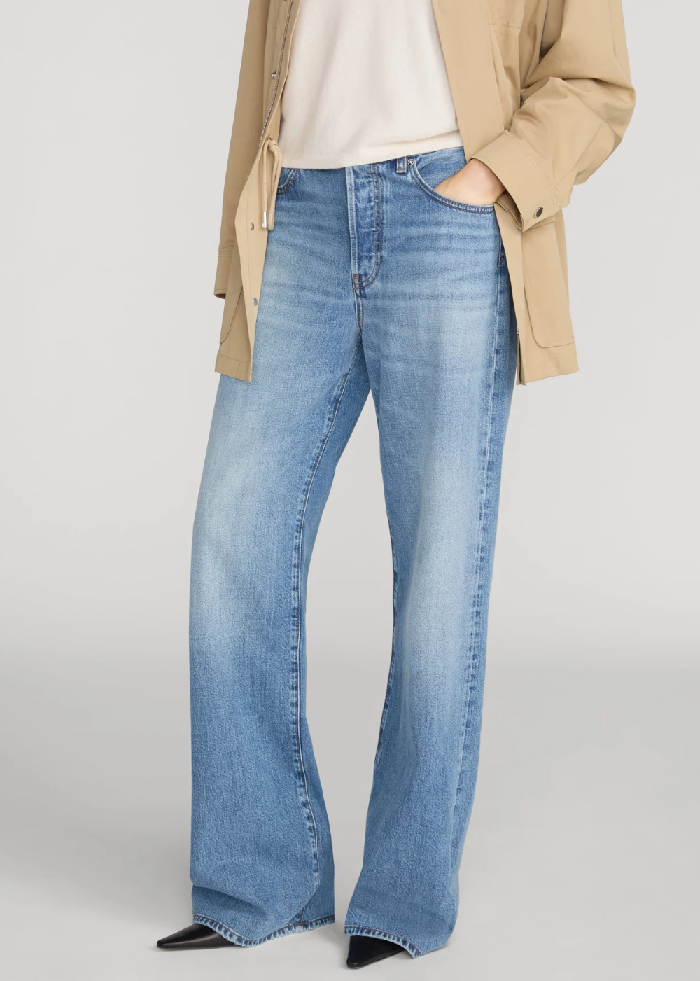 A person wearing light-wash blue wide-leg jeans with a beige blazer and white top, shown from the chest down against a light gray studio background.