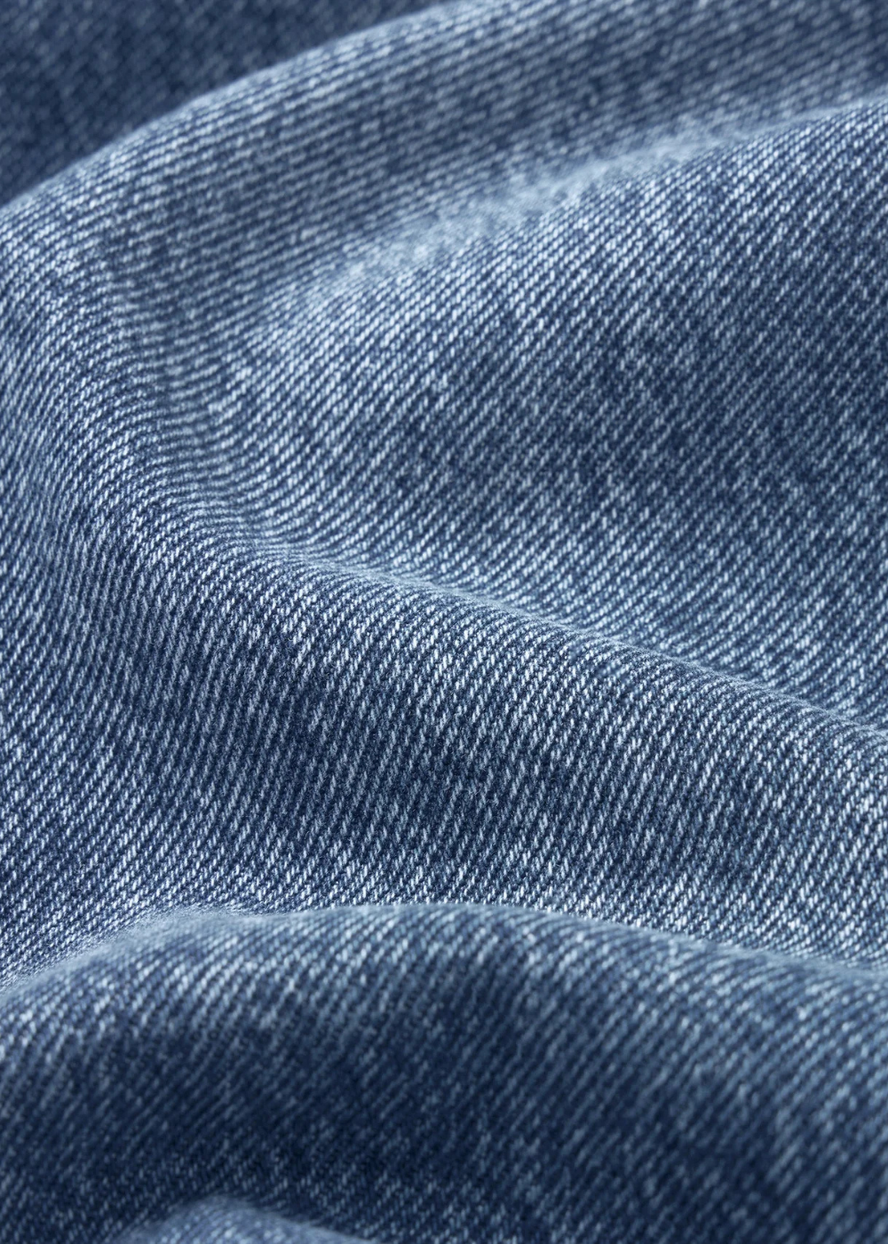 A close-up of blue denim fabric with visible twill texture and soft folds.