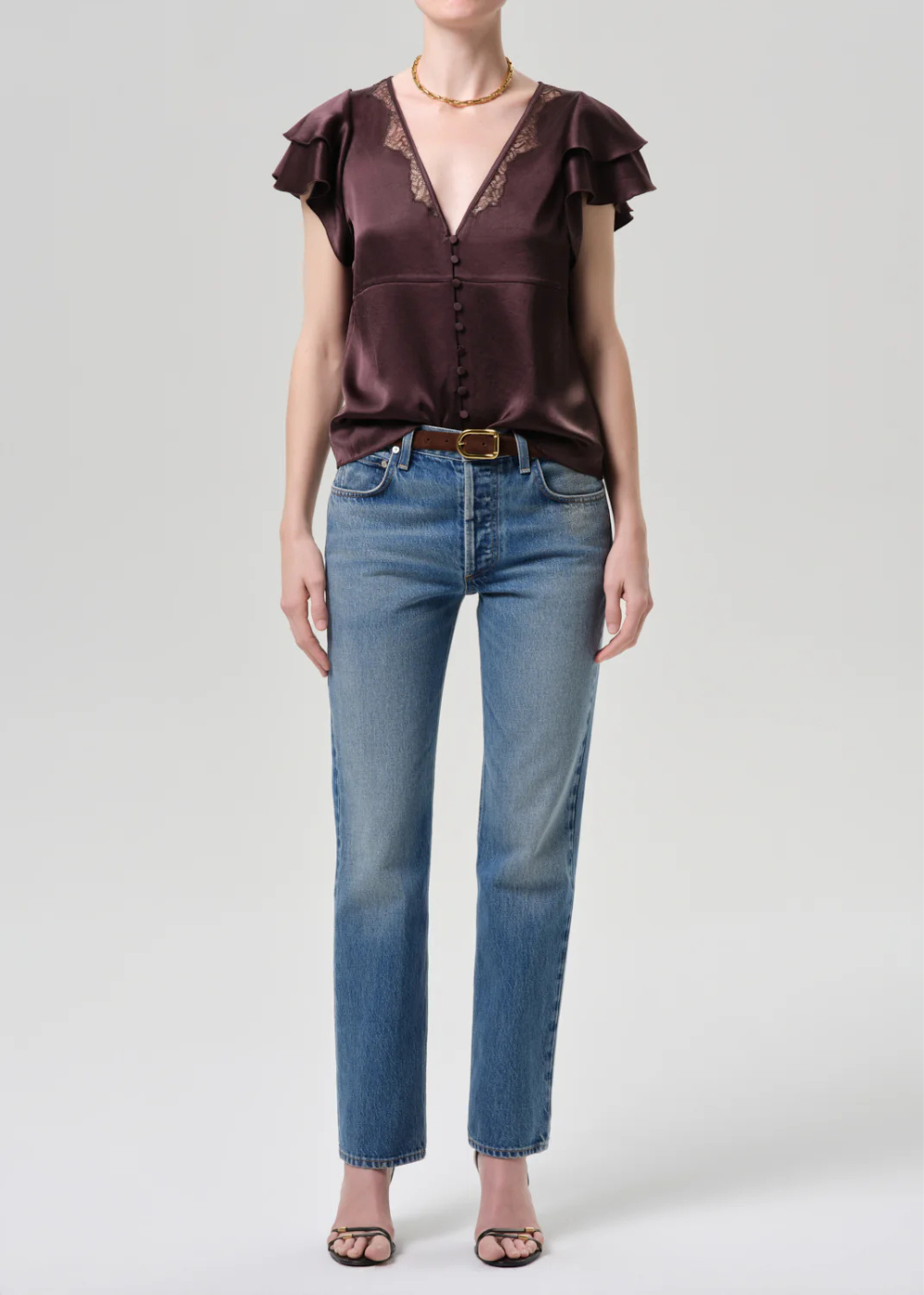 Woman wearing a brown satin blouse with ruffled sleeves and blue jeans on a light gray background
