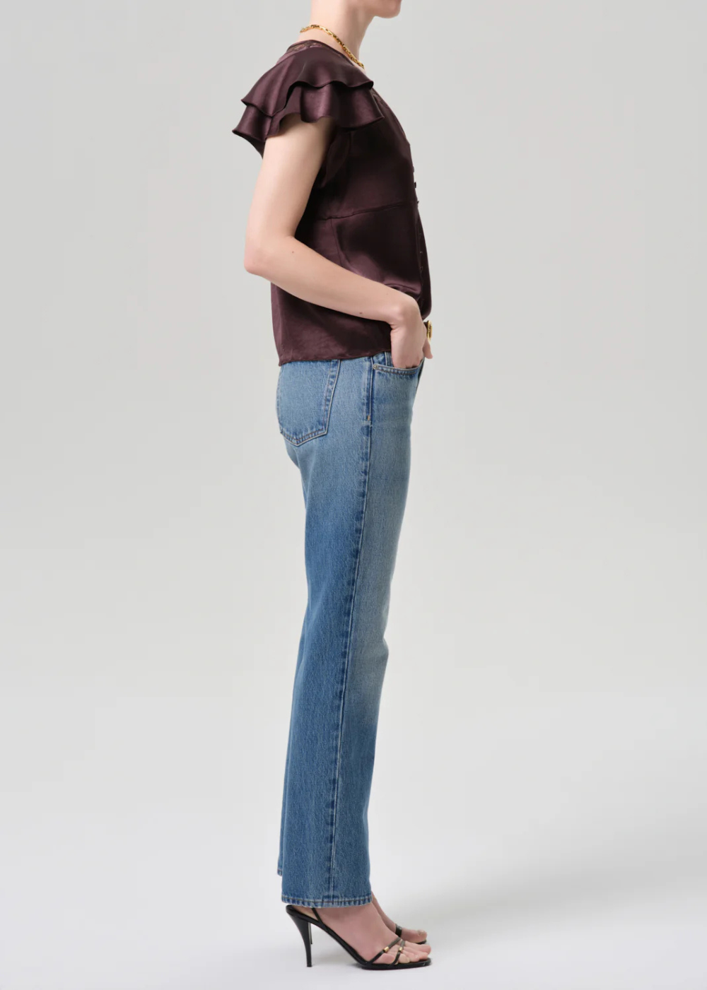 Person wearing a brown top with ruffled sleeves and blue jeans on a light gray background