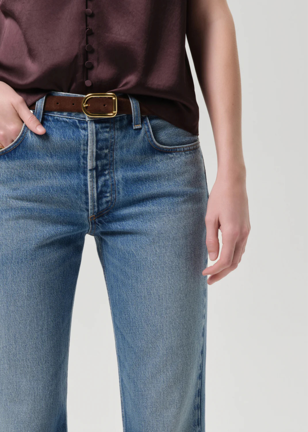 Person wearing blue jeans with a brown belt on a plain background