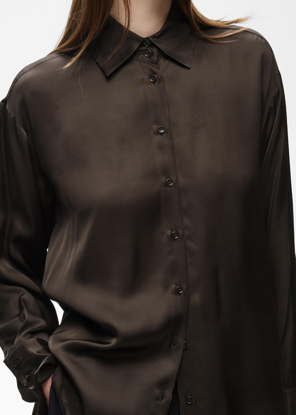 A close-up of a model wearing a dark brown, semi-sheer satin button-down shirt with a pointed collar.