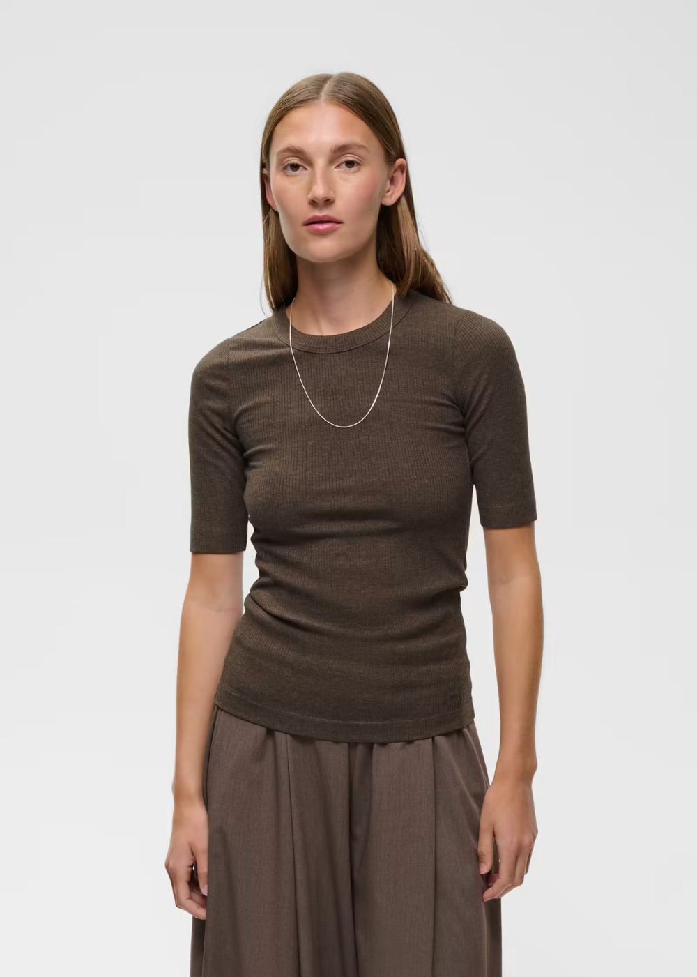 A woman modeling a short-sleeve crewneck knit top in a dark brown color, paired with matching brown wide-leg trousers, against a light gray studio background.