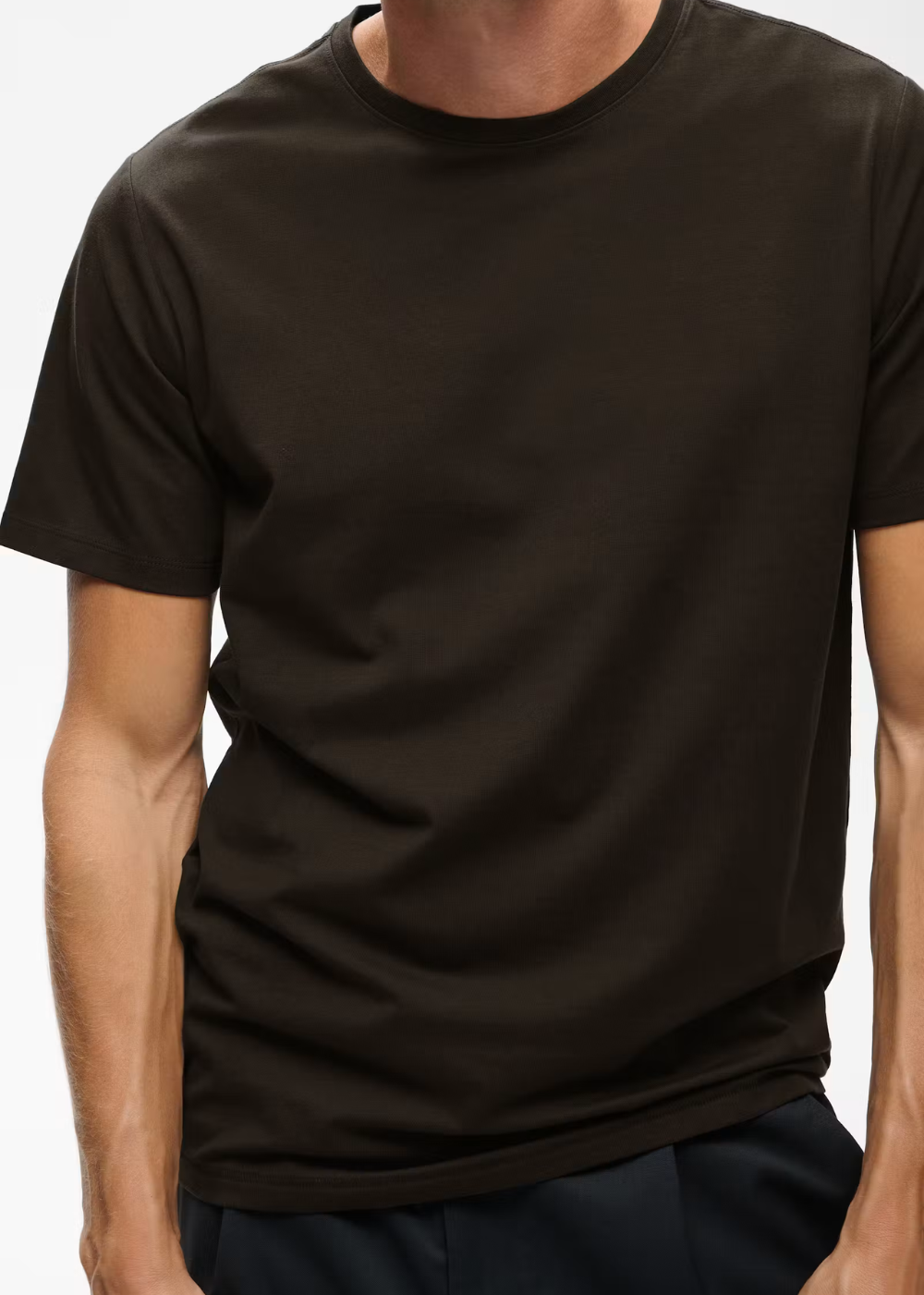 A man wearing a plain dark brown short-sleeve crewneck t-shirt, cropped from the neck down, against a light gray background.