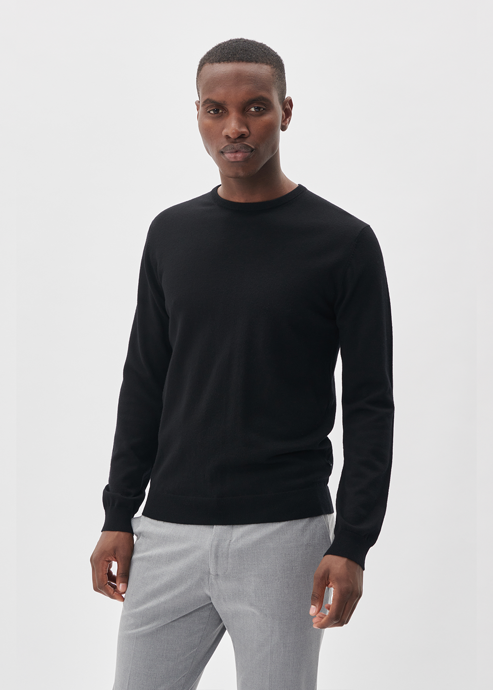 Man wearing a black long-sleeve shirt and light gray pants on a white background