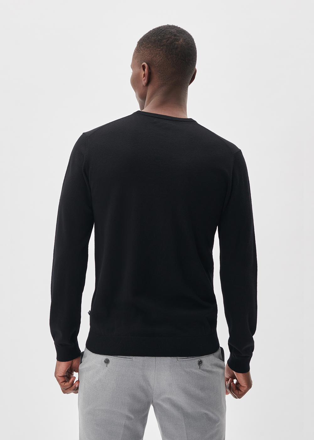 Man wearing a black sweater and light gray pants on a white background