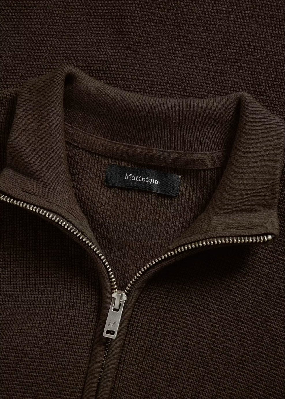Close-up of a dark brown ribbed knit quarter-zip sweater with a stand collar and a black Matinlèe brand label at the neck.