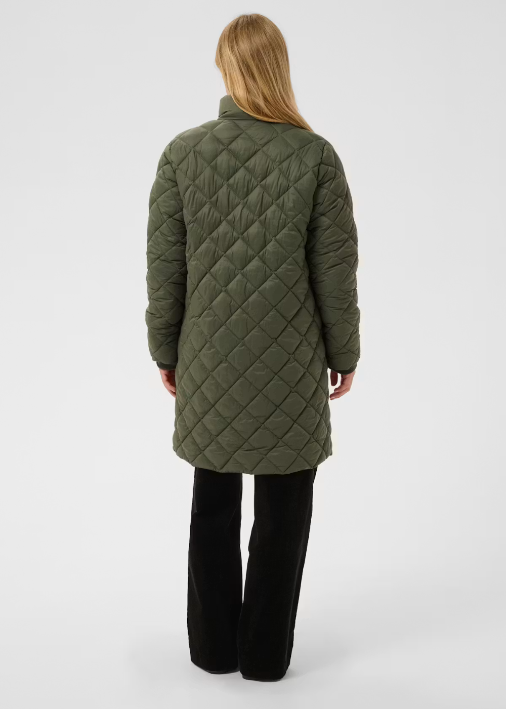 A woman viewed from the back wearing a quilted olive green coat and black wide-leg trousers, standing against a light gray studio background.