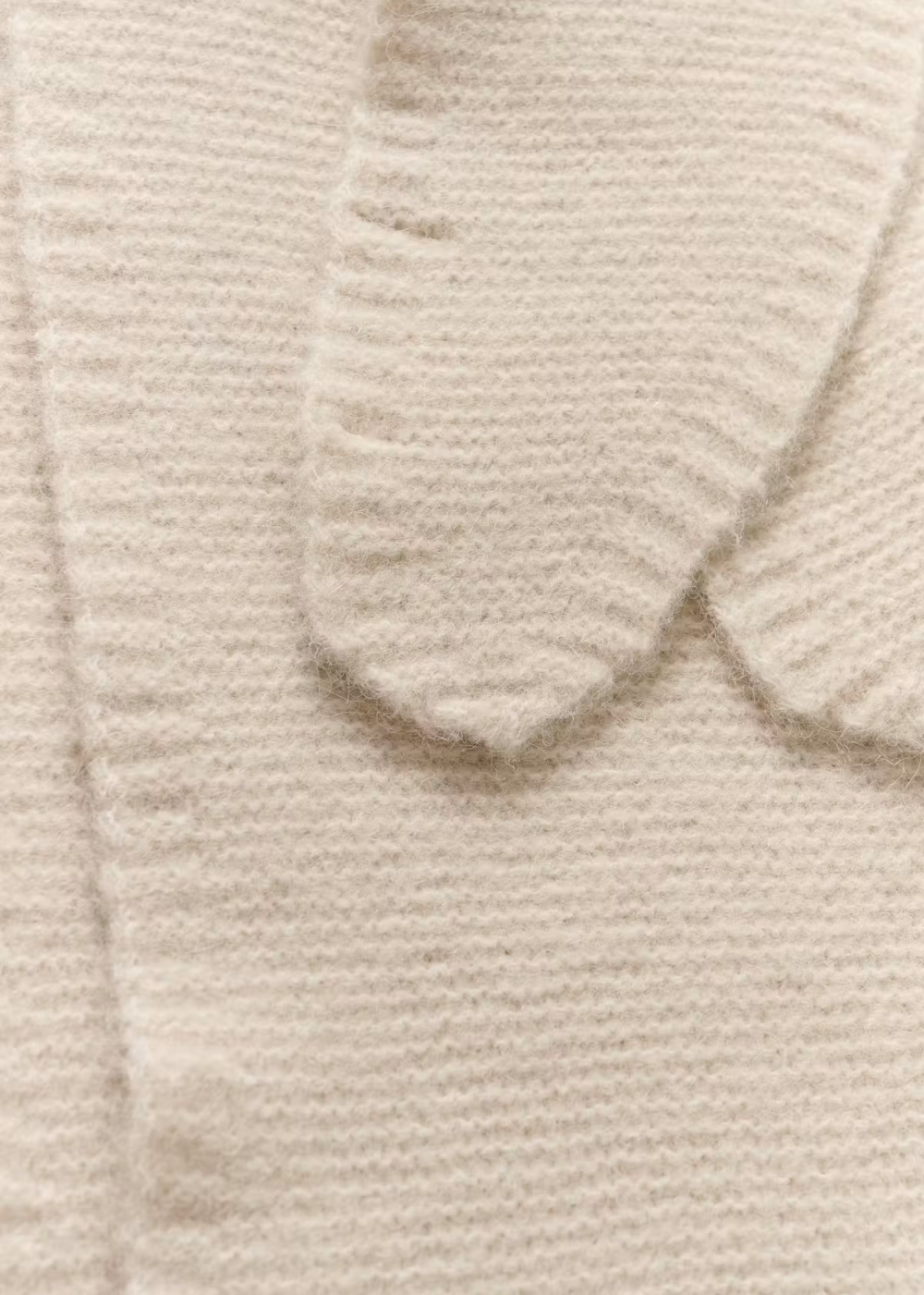 Close-up of a cream-colored knit fabric with a ribbed texture and a folded cuff detail.