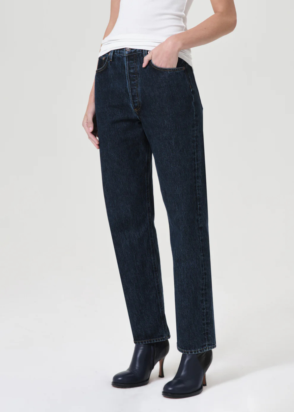 Person wearing dark blue jeans and black boots on a white background