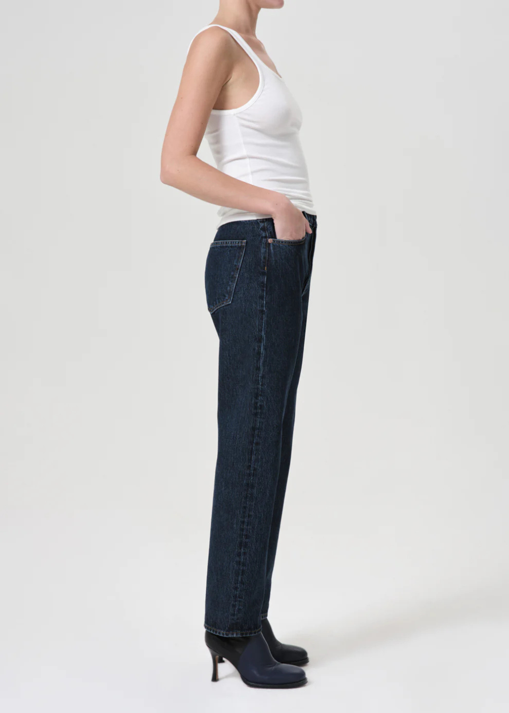 Person wearing a white tank top and dark blue jeans on a plain background