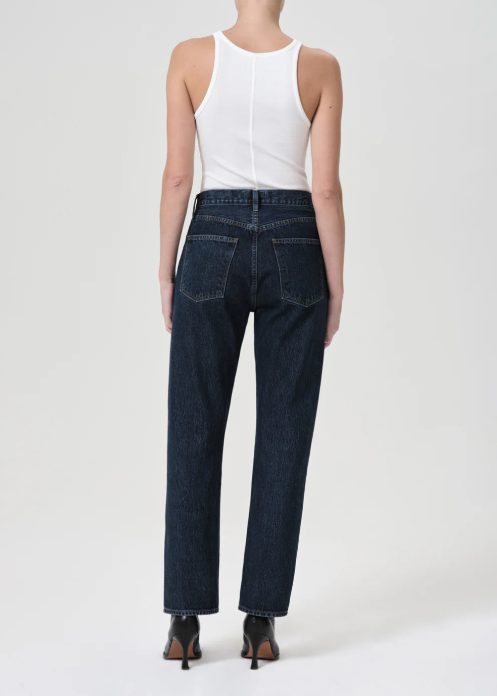 Person wearing dark blue jeans and a white top on a white background