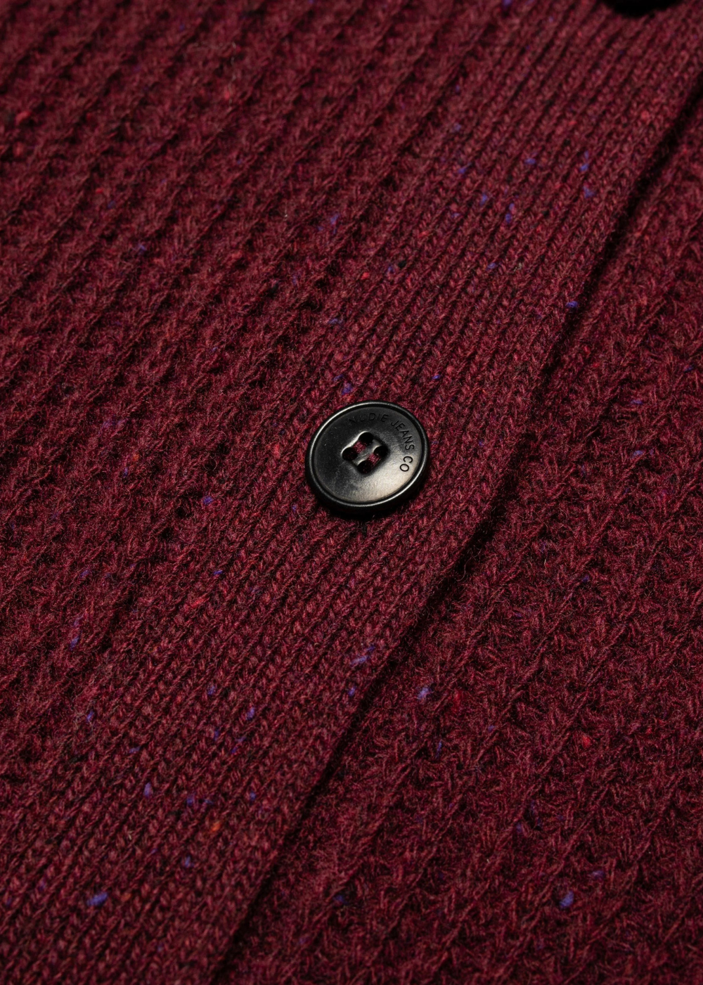 Close-up of a dark burgundy ribbed knit cardigan with a single black button, showing the heathered texture of the fabric.
