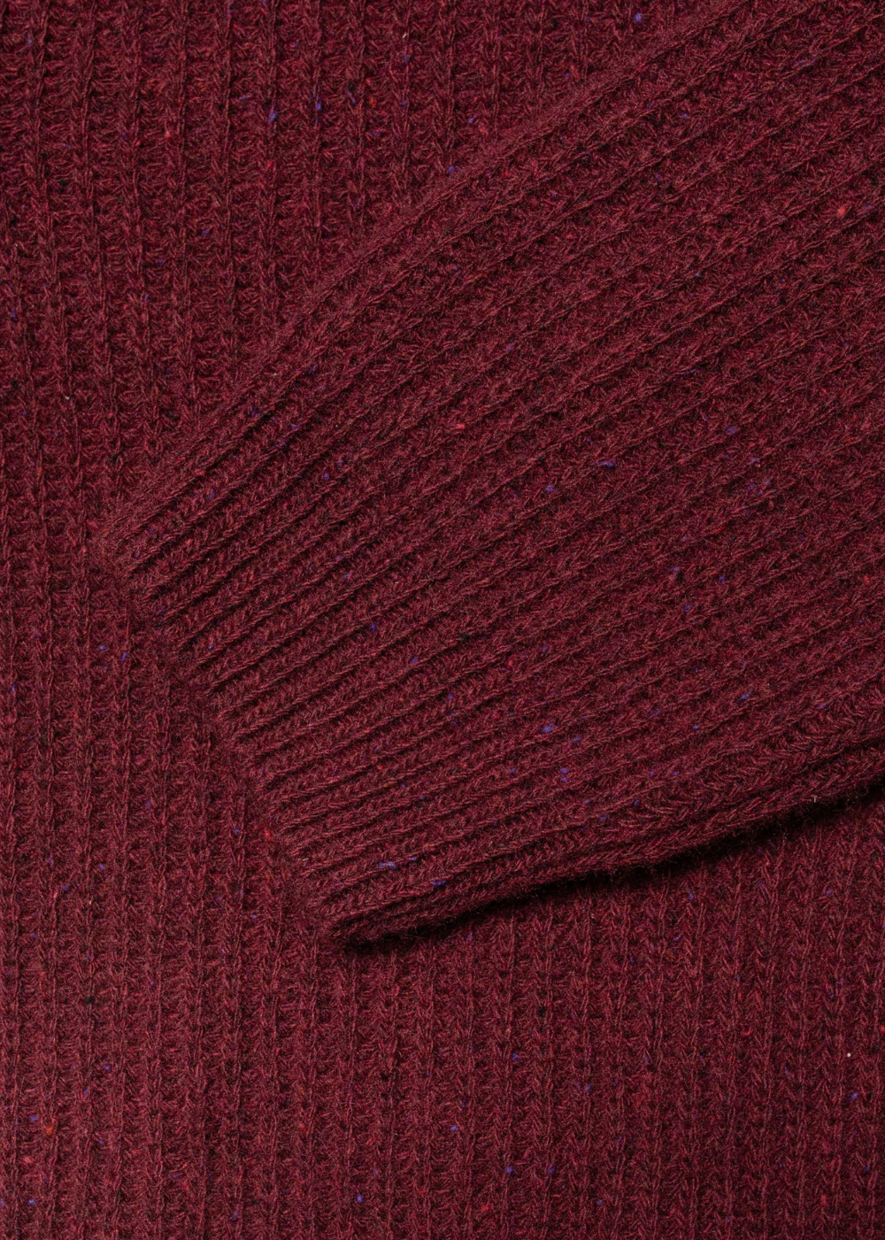 Close-up of a ribbed knit sweater in a deep burgundy red, showing the texture and a folded cuff detail.