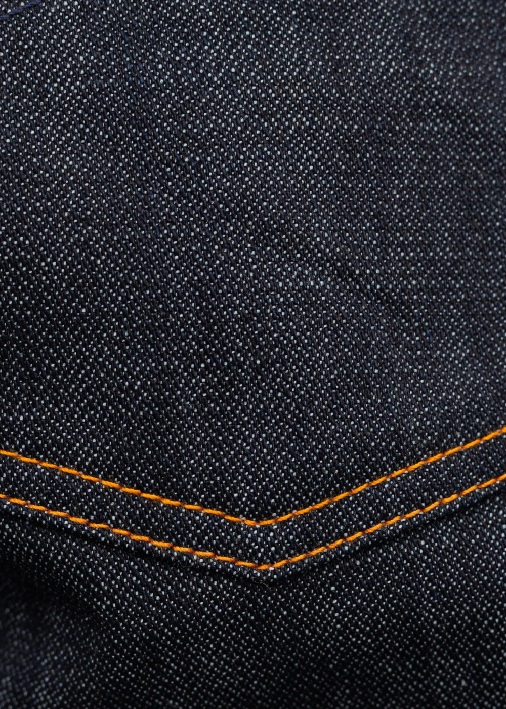 Close-up of dark indigo denim fabric with orange contrast stitching along a folded seam.