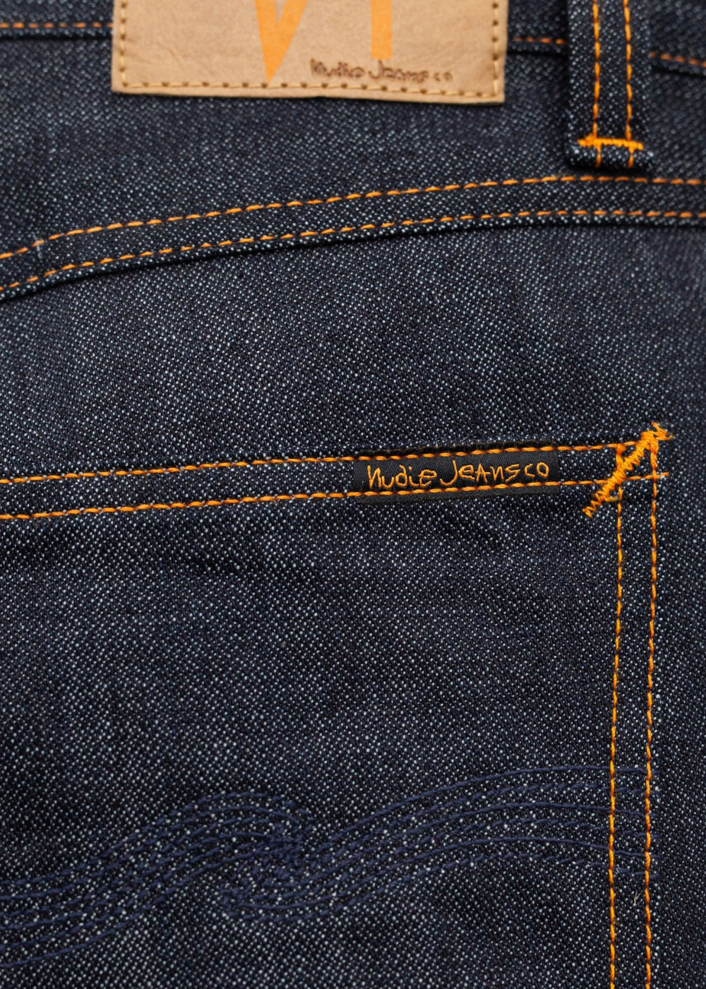 Close-up of dark indigo denim jeans showing the back pocket with orange contrast stitching, a tan leather patch, and 'Nudie Jeans Co' embroidered on the pocket.