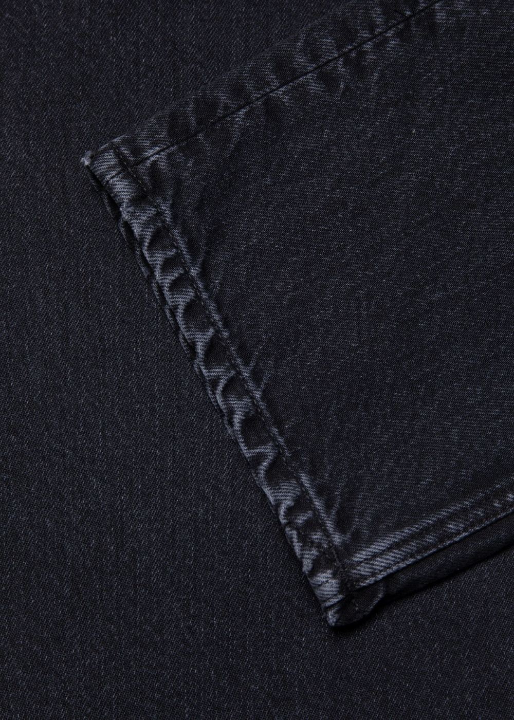 Close-up of a black denim fabric corner showing a neatly finished double-stitched seam.