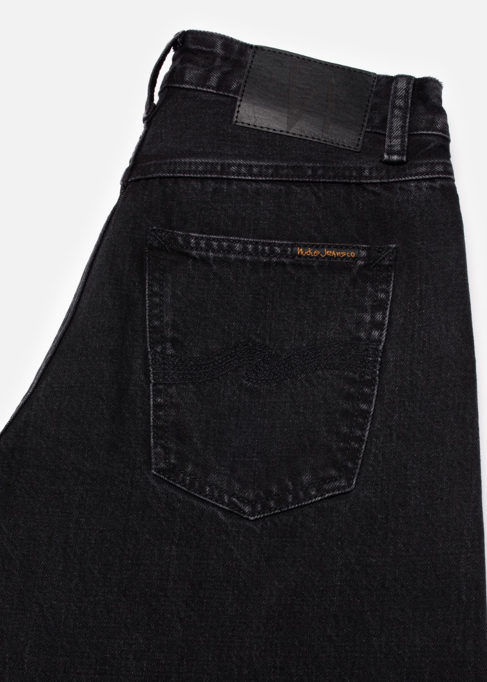 Close-up of the back waistband and right rear pocket of black denim jeans, showing a small gold-tone ROKA brand label on the pocket.