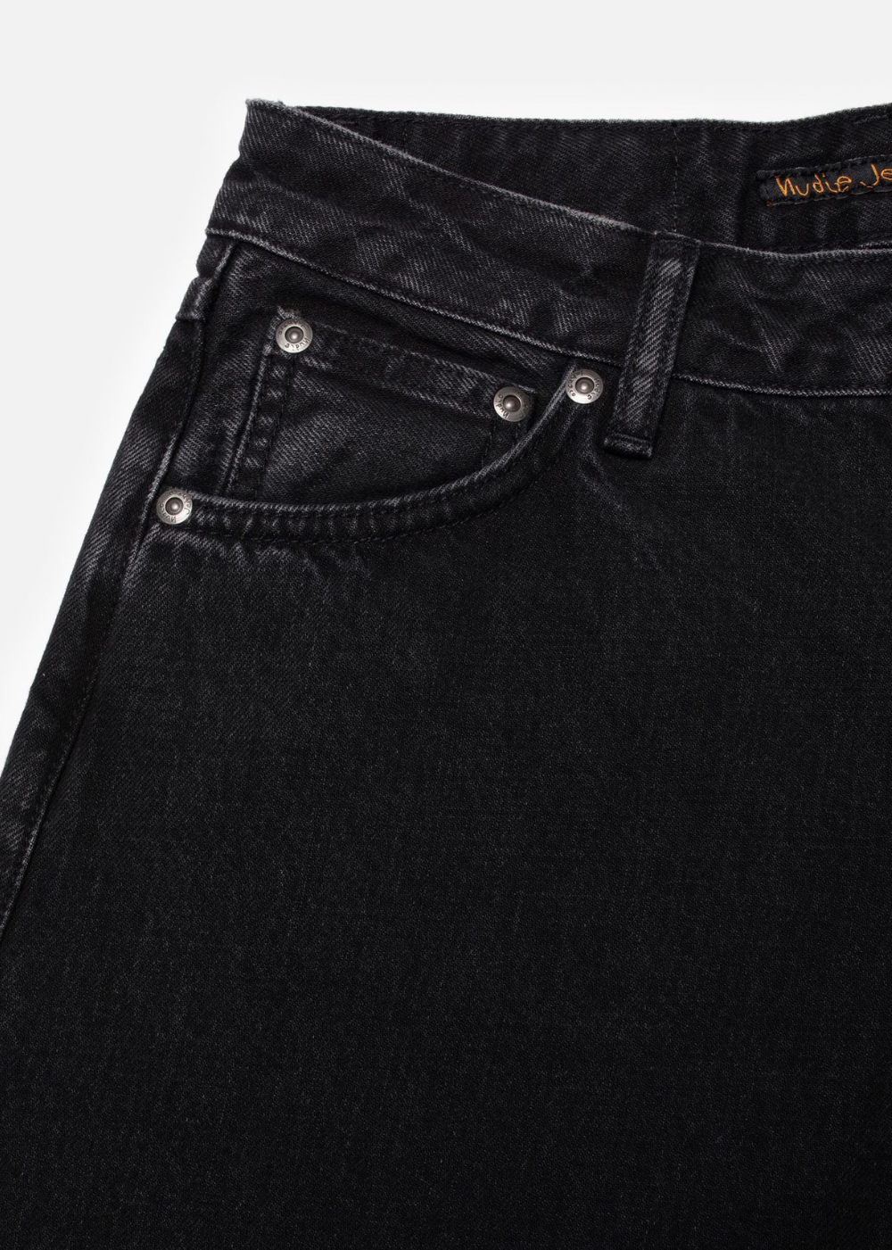 Close-up of black denim jeans showing the waistband, belt loops, front pocket, and silver rivets on a light gray background.