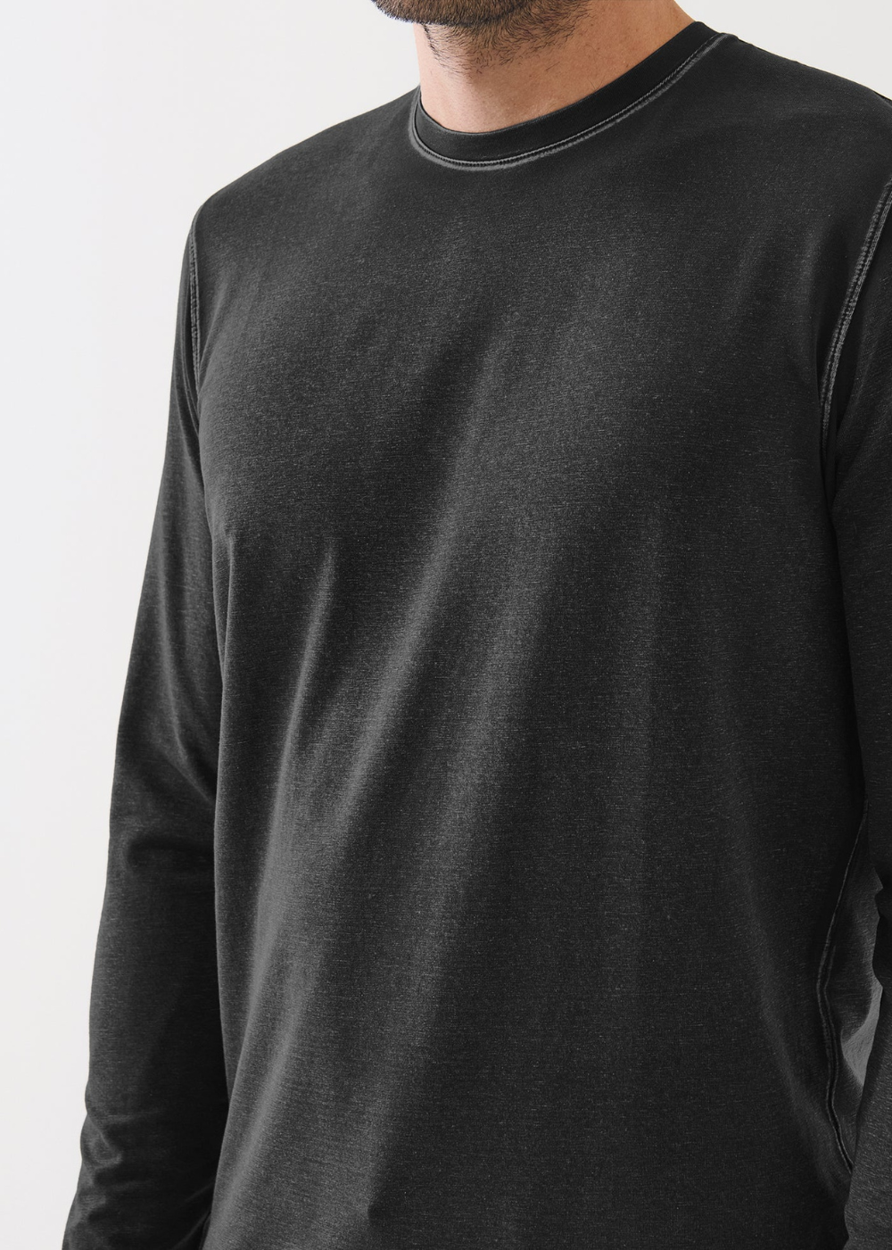 A close-up of a man wearing a dark charcoal gray long-sleeve crewneck shirt, showing the fabric texture and collar detail against a plain light background.