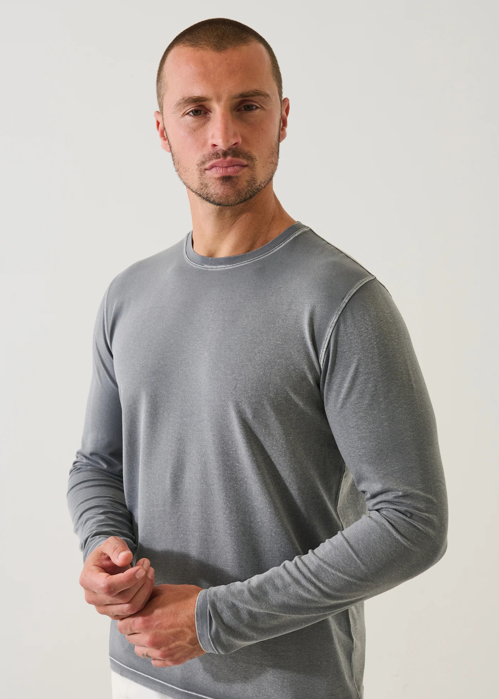 A man wearing a plain gray long-sleeve crewneck shirt, standing against a light gray studio background.