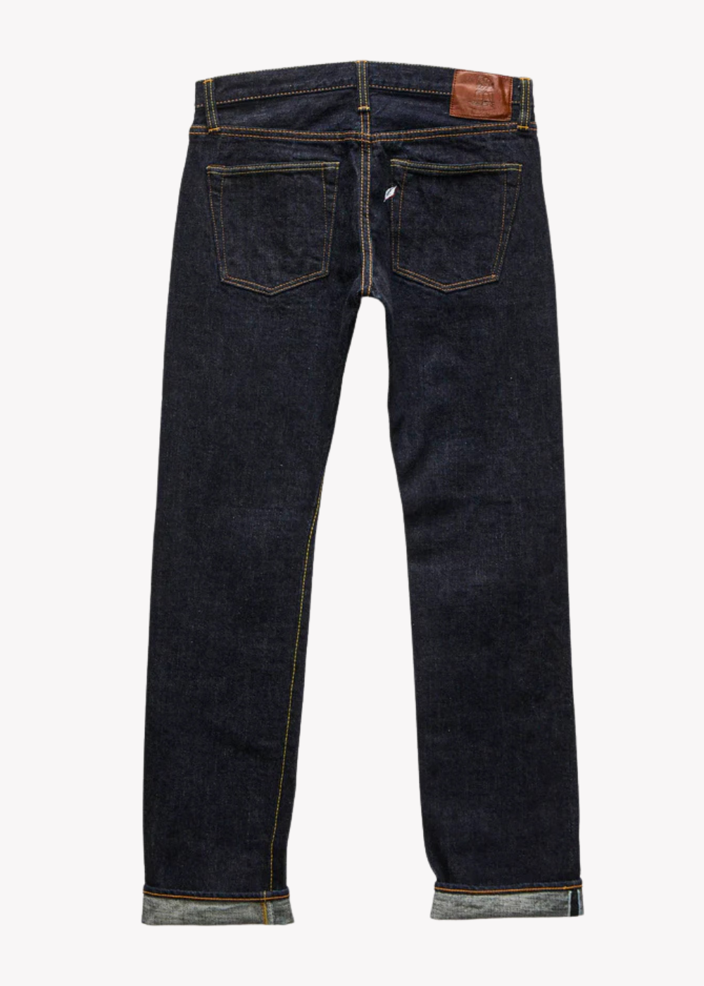 Back view of dark indigo denim jeans with rolled cuffs, showing the back pockets and a brown leather patch on the waistband, set against a plain white background.