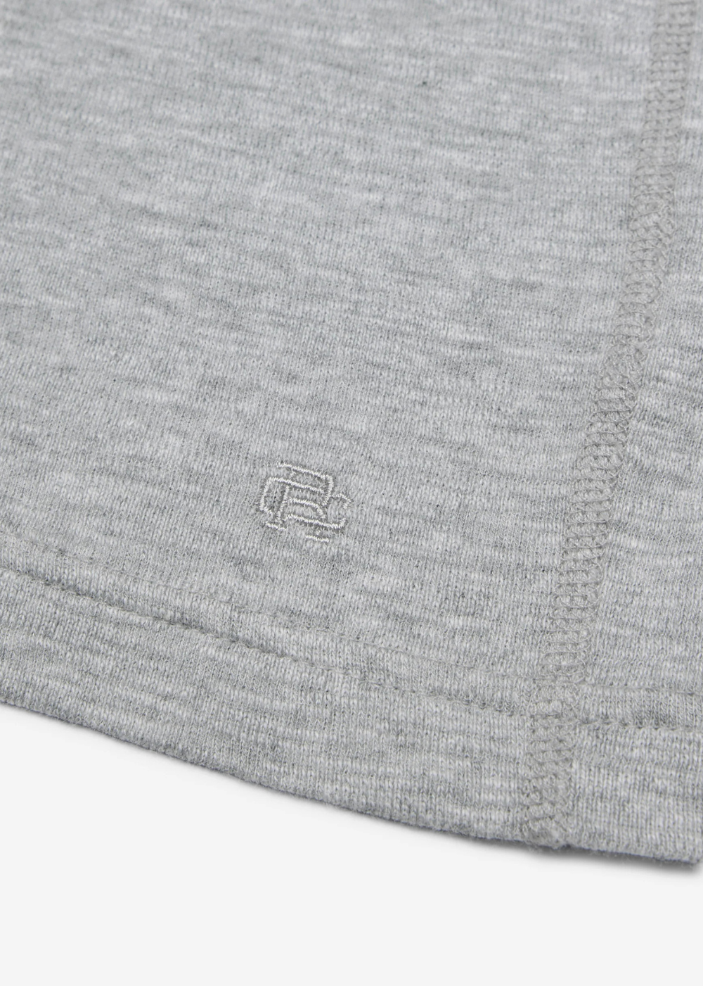 Close-up of a light gray heather knit fabric with a small tonal embroidered logo near the lower center, showing ribbed hem and stitched edge details.