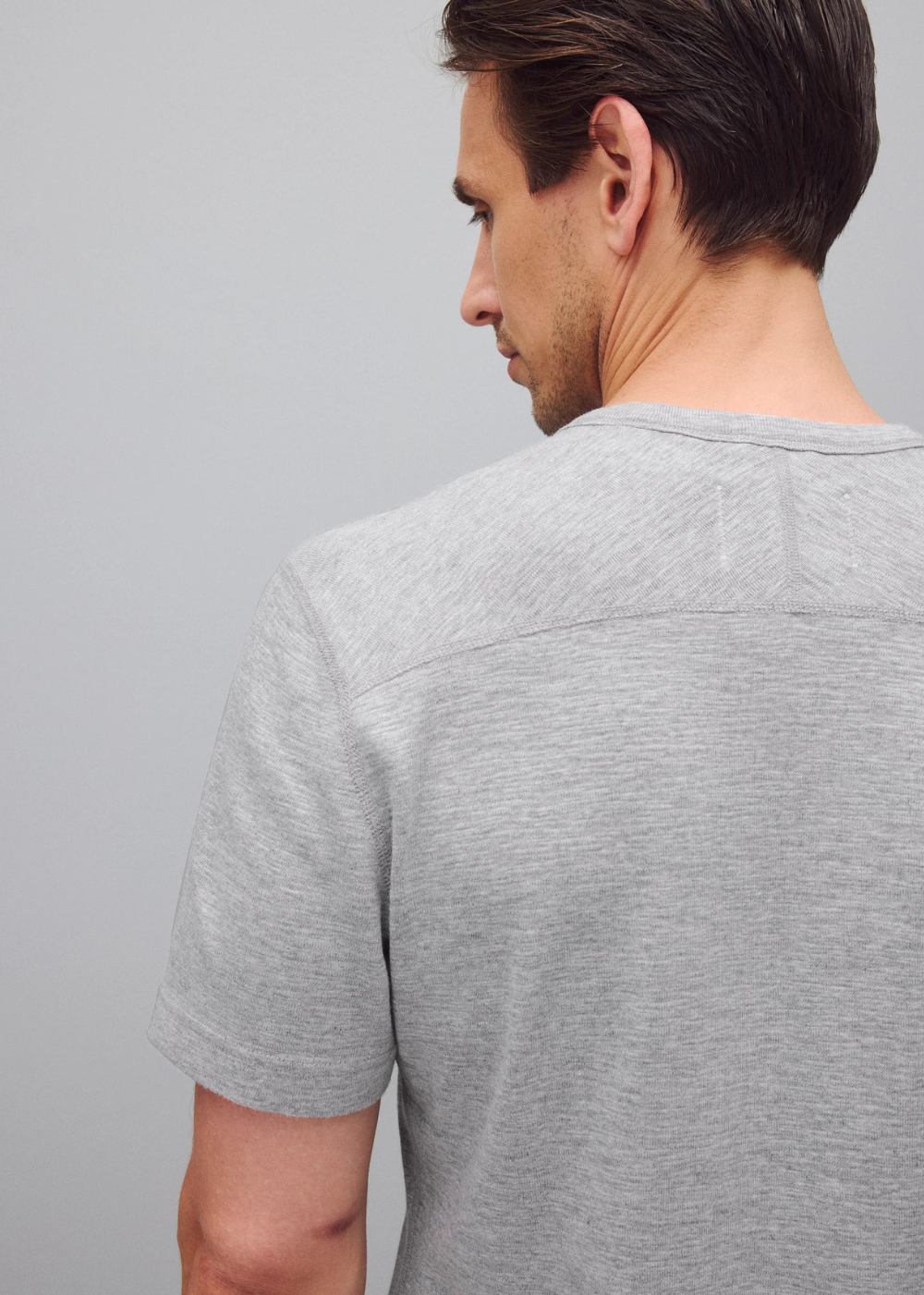 A man shown from the back wearing a light gray short-sleeve crewneck t-shirt against a solid gray background.