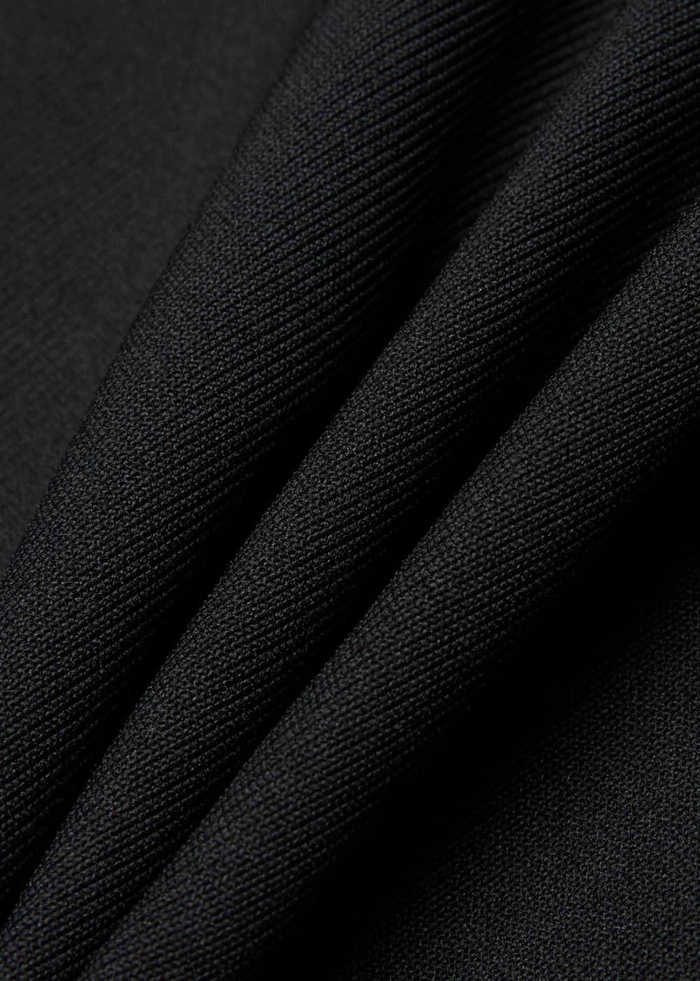 A close-up of black textured fabric with soft diagonal folds showing the woven material detail.