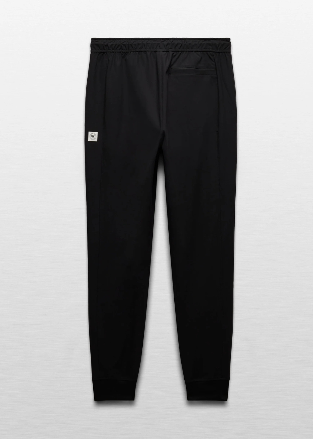 Black jogger pants with an elastic waistband and a small white square logo patch on the left thigh, shown against a light gray background.